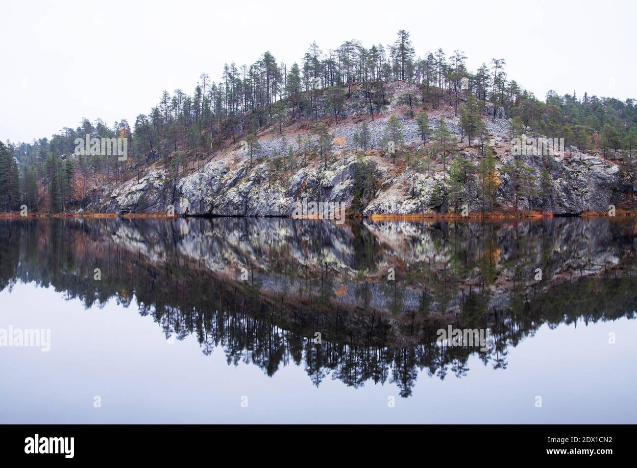 Eine Spiegelung einer felsigen Klippe, die von Pinien bedeckt ist, an einem Herbstnachmittag im Oulanka-Nationalpark in Nordfinnland. Stockfoto