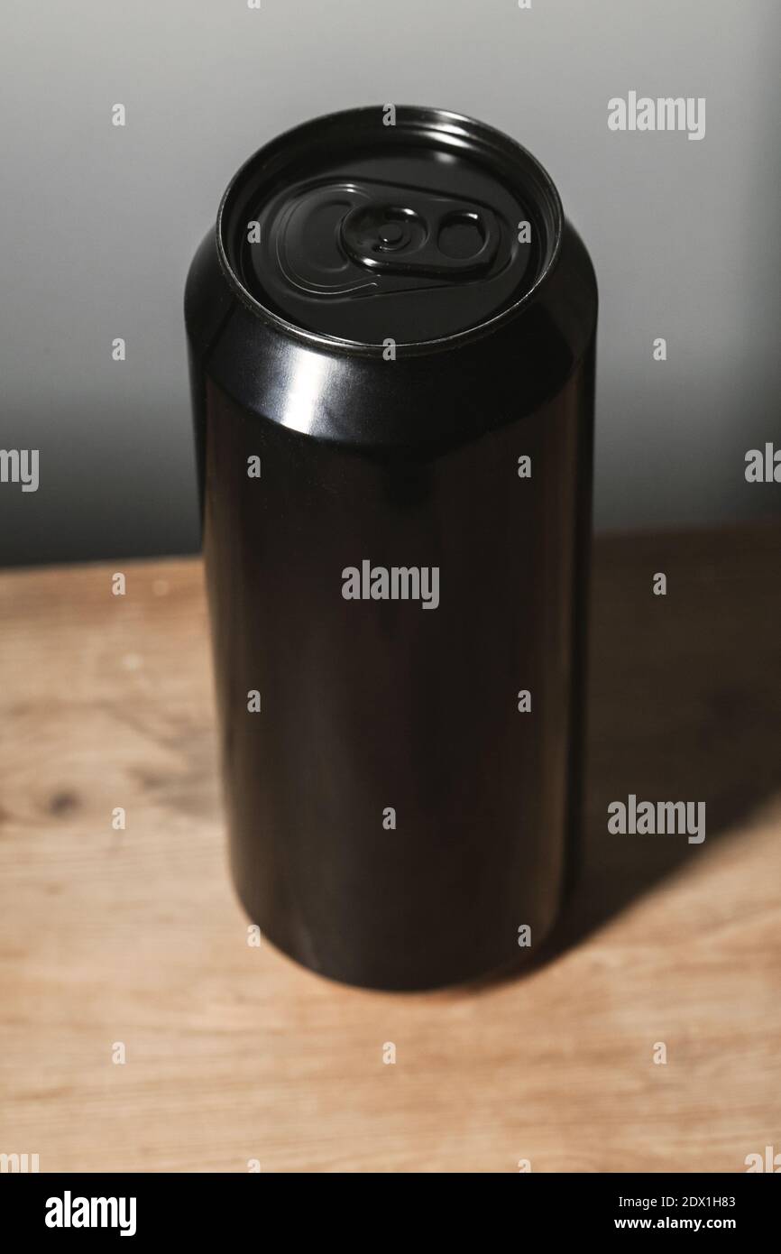 Geschlossene glänzende schwarze Aluminium-Dose steht auf einem Holztisch, Standard-Softdrink-Verpackung. Vertikales Foto Stockfoto