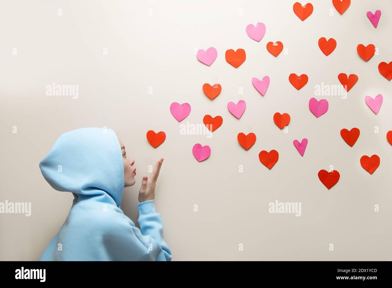 Young Girl im blauen Hoodie mit Kapuze bläst Herzen von ihrer Handfläche und sie fliegen, kopieren Raum. Valentinstag, Suche Liebe Konzept, gute geben Stockfoto