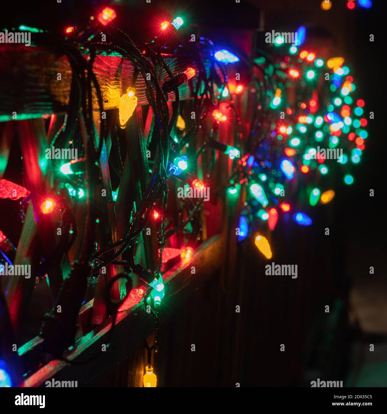 Quadratisches Foto von Real Blurry Christmas Multicolored Lichter auf hölzernen Terrassenzaun. Viele blinkende Lampen, die nacheinander Farbe ändert. Neujahr und C Stockfoto