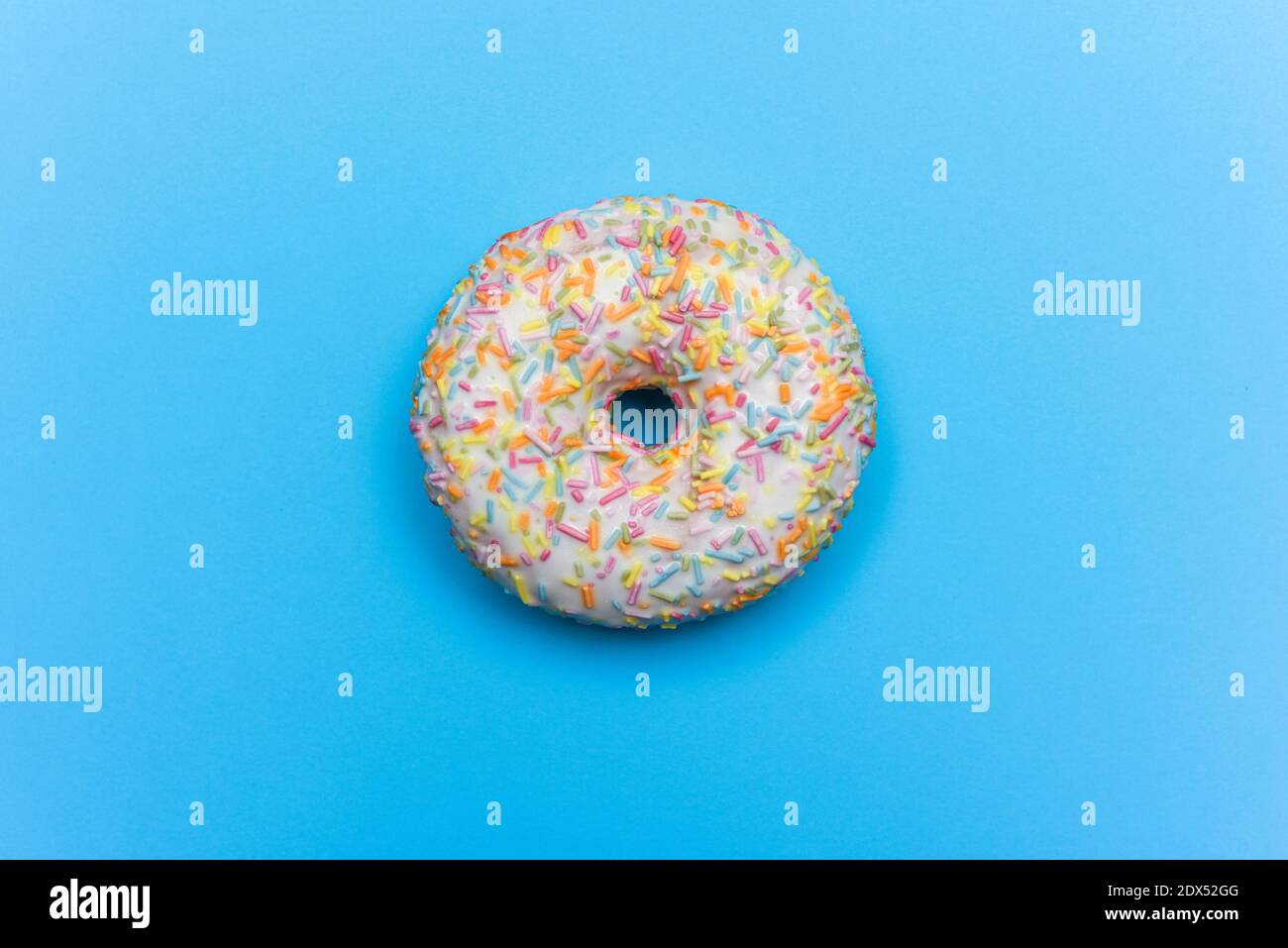 Glasiert und dekoriert Eistonut mit weißem Zuckerguss und farbig Sprikles isoliert auf blauem Hintergrund Stockfoto