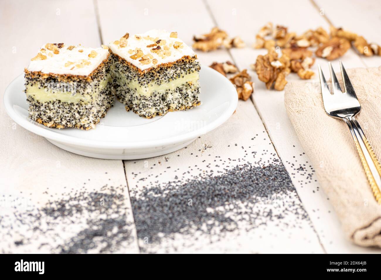 Mohnkuchen mit cremiger Füllung und Walnüssen auf dem Dessert. Serviert auf einem weißen Retro-Holztisch in goldener Form in warmen Farben. Hausgemachtes Dessert. Stockfoto