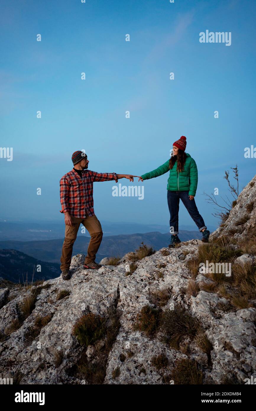 Wanderpaar berührt die Finger, während sie auf einem felsigen Berg stehen Blauer Himmel Stockfoto