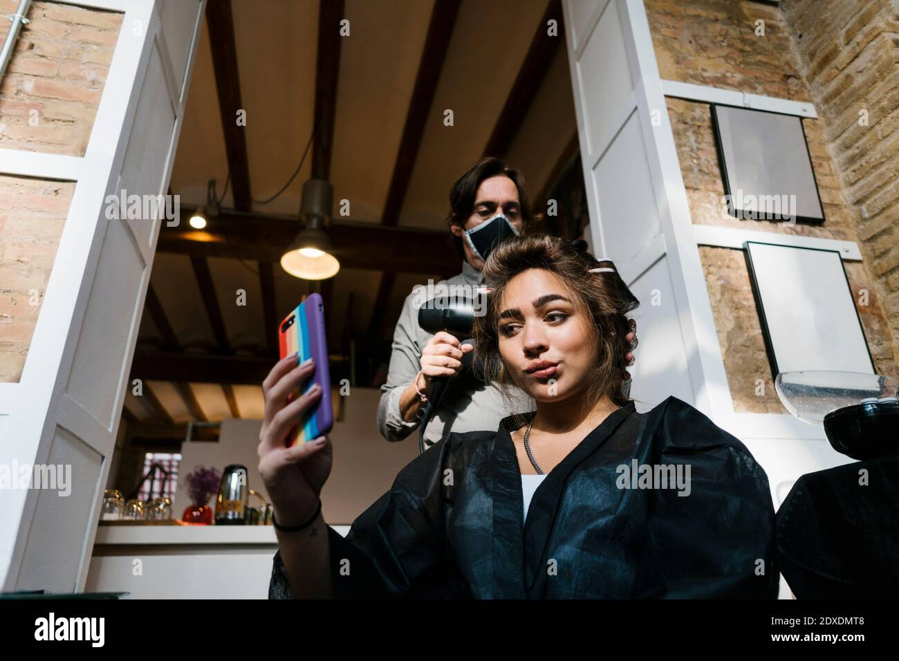 Männlich Friseur Trocknen Teenager-Mädchen Haare während der Aufnahme Selfie auf Smartphone im Salon Stockfoto