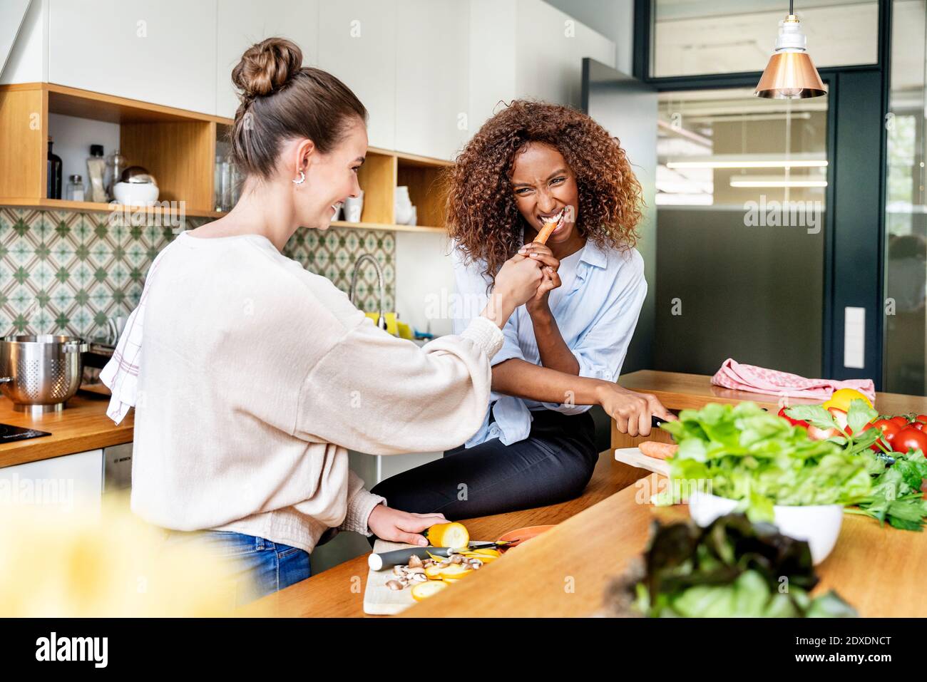 Geschäftsfrau essen Karotte von Kollegen während der Zubereitung von Lebensmitteln im Büro Küche Stockfoto
