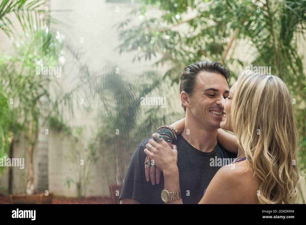 Liebevolles junges Paar nuzzling Nase beim Umarmen gegen Pflanzen in Hinterhof Stockfoto