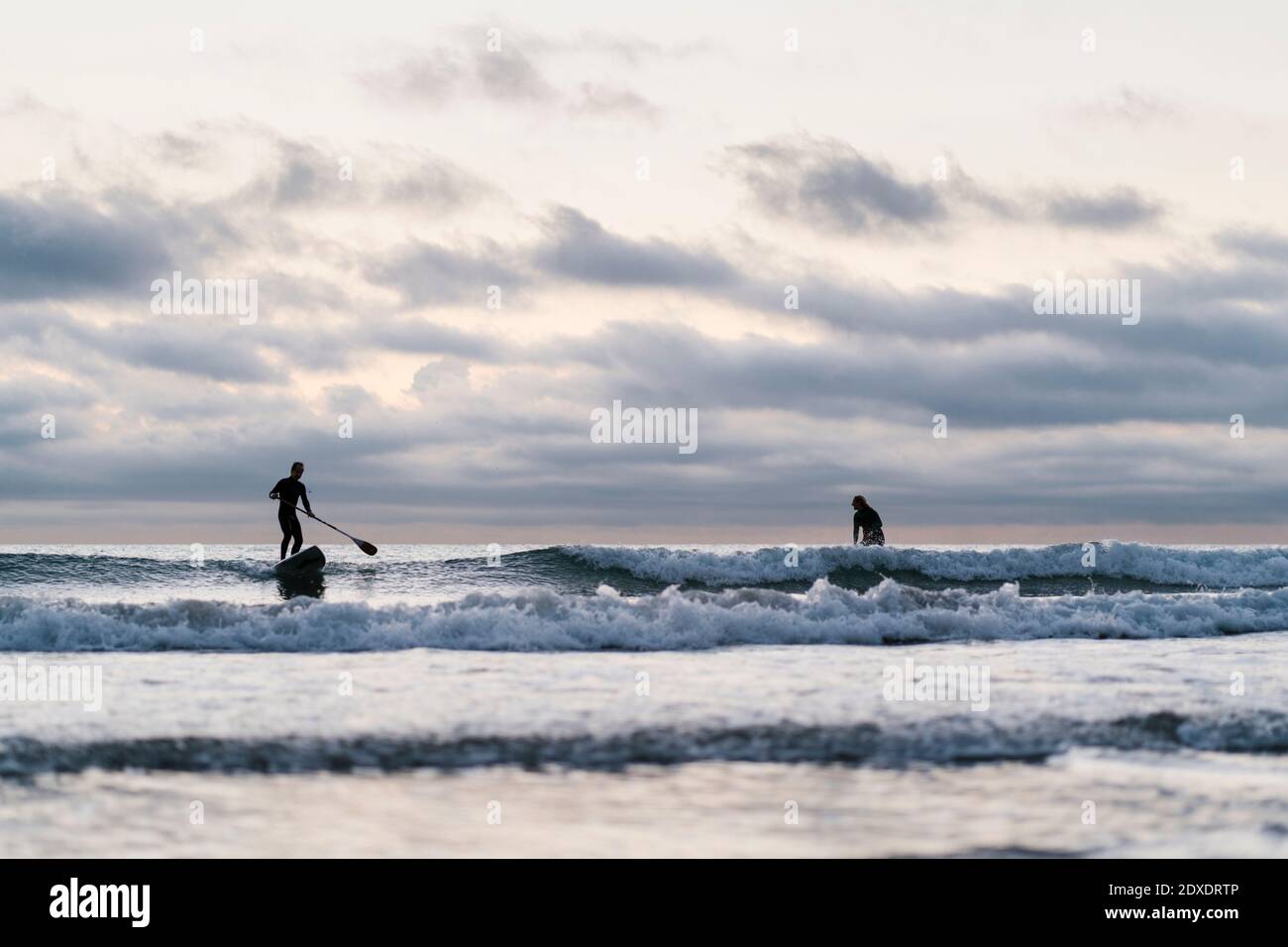 Freunde surfen mit Paddleboard auf dem Meer gegen den Himmel während der Dämmerung Stockfoto