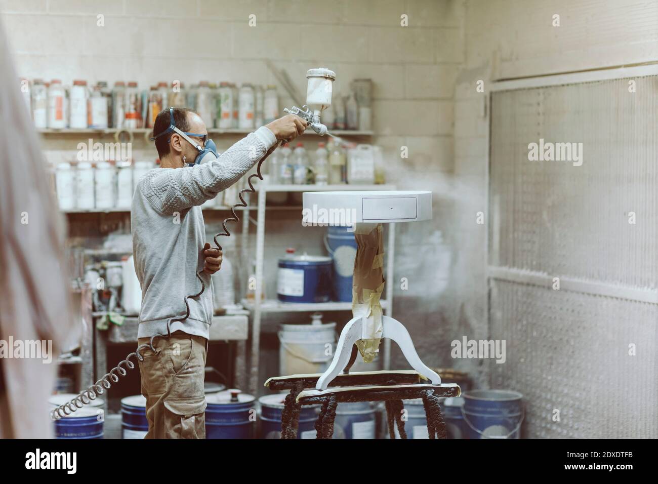 Zimmermann trägt Gesichtsmaske Malerei Tisch mit Spritzpistole an Werkstatt Stockfoto