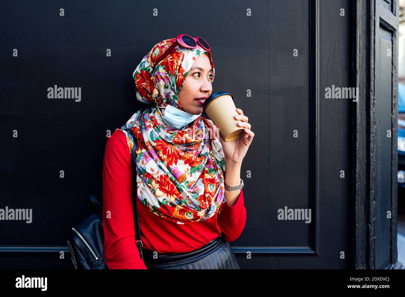 Muslimische Frau beim Kaffee trinken gegen schwarze Wand während COVID-19 Stockfoto