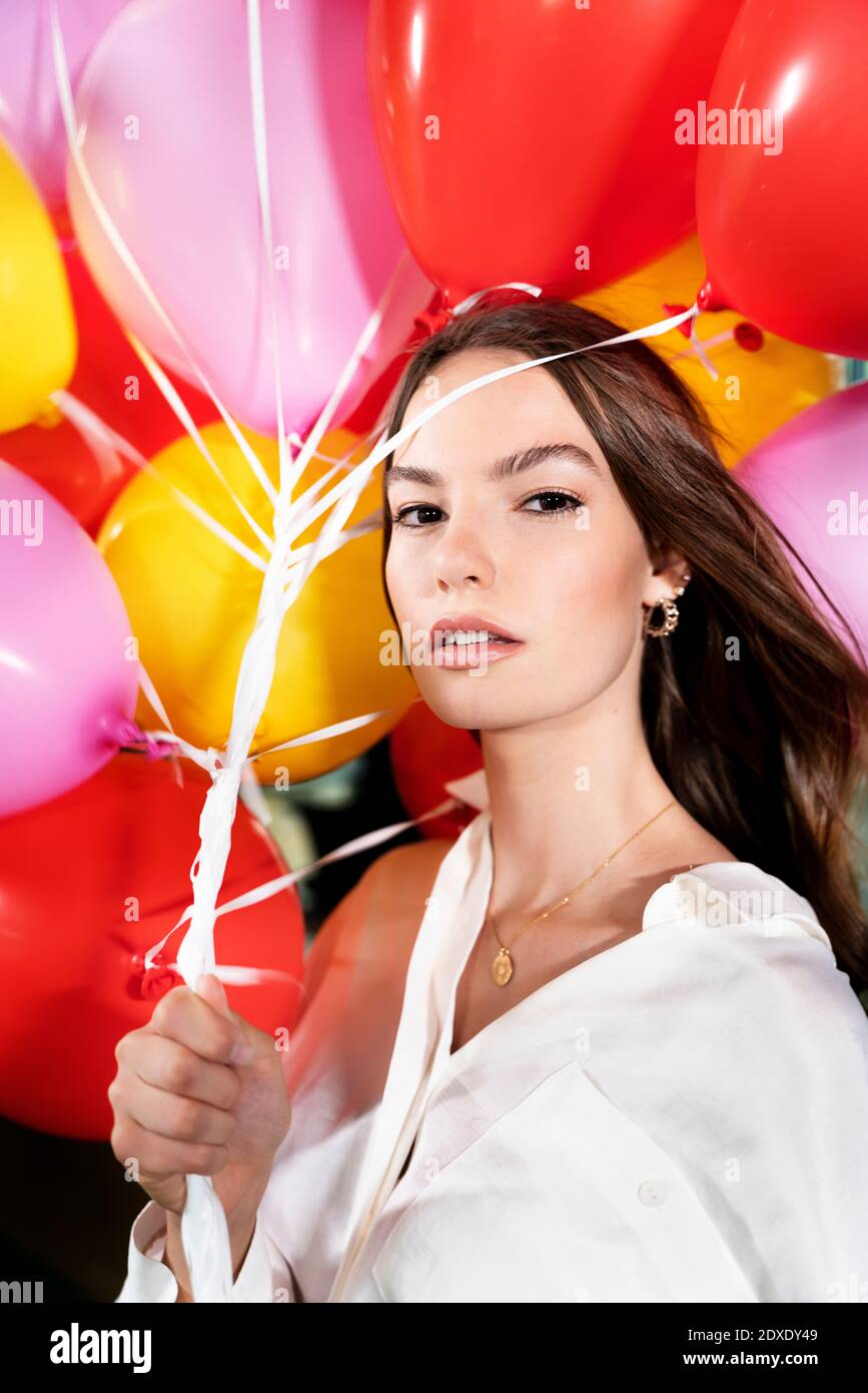 Junge Geschäftsfrau starrt, während sie den Mehrfarbenballon im Büro hält Stockfoto
