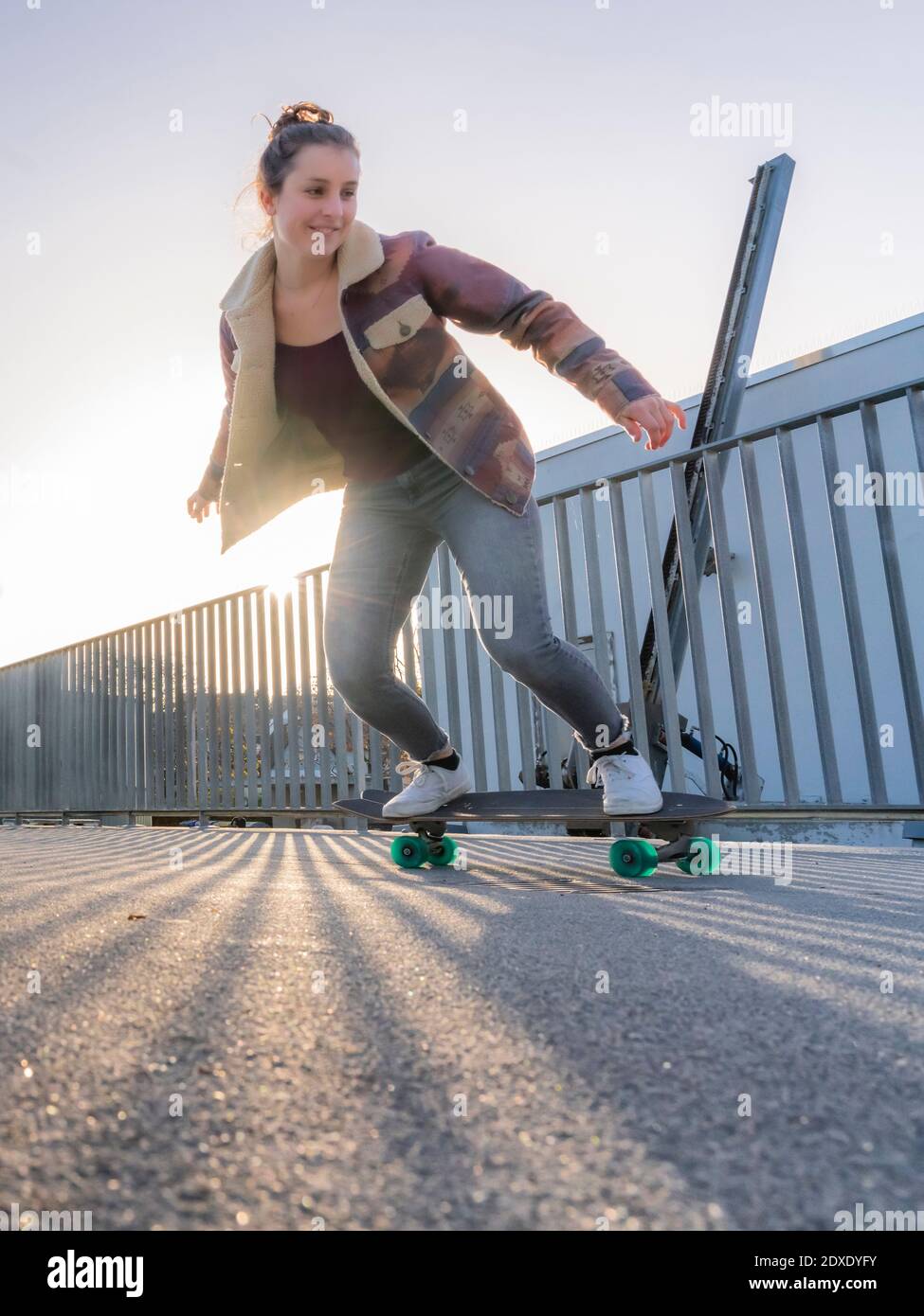 Junge Frau mit coolem Attitude Skateboarding auf Fußgängerbrücke bei Sonnenuntergang Stockfoto