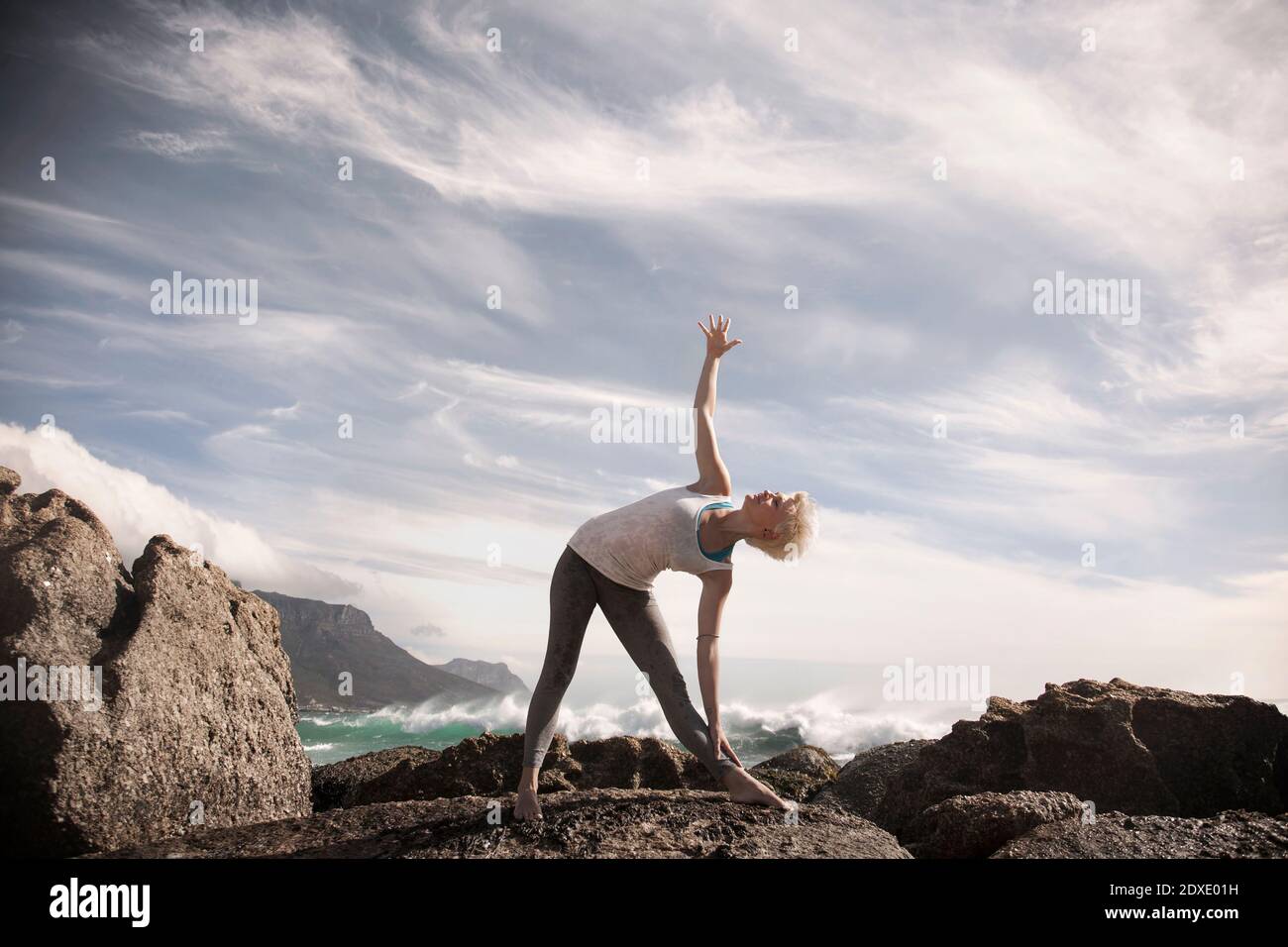 Frau übt Trikonasana auf Felsformation gegen Himmel Stockfoto