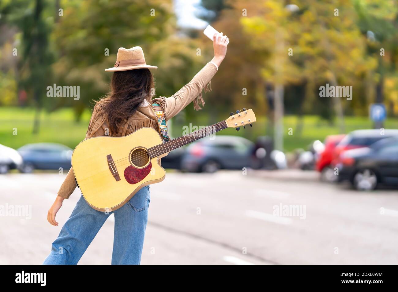 Junge Frau mit Gitarre winkt Hand zu Taxi auf der Straße Stockfoto