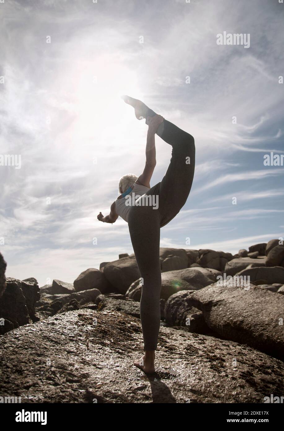 Flexible Frau praktiziert Natarajasana auf Felsformation am Strand Stockfoto