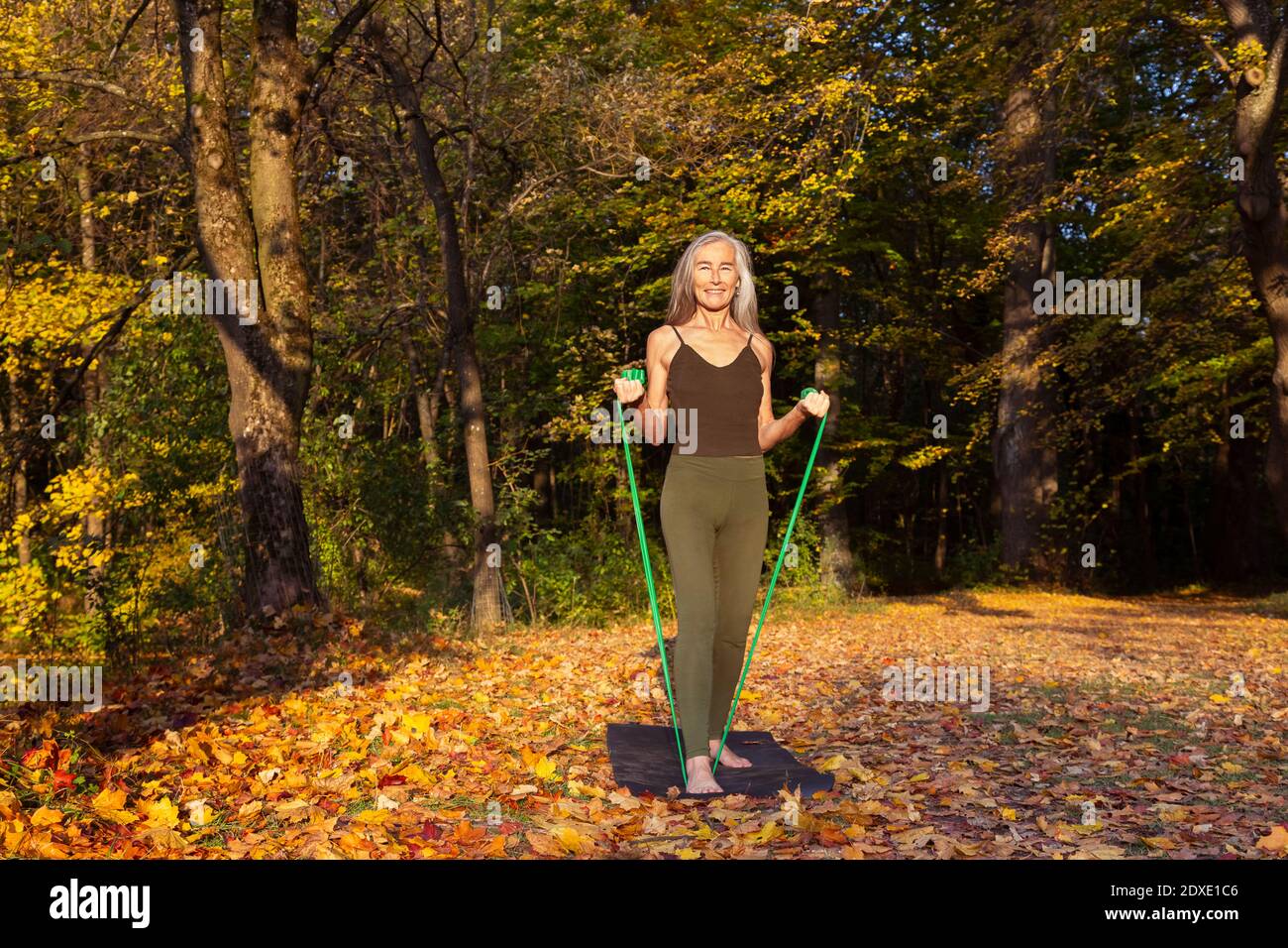 Lächelnde Frau beim Training mit Widerstandsband auf Matte im Park Im Herbst Stockfoto
