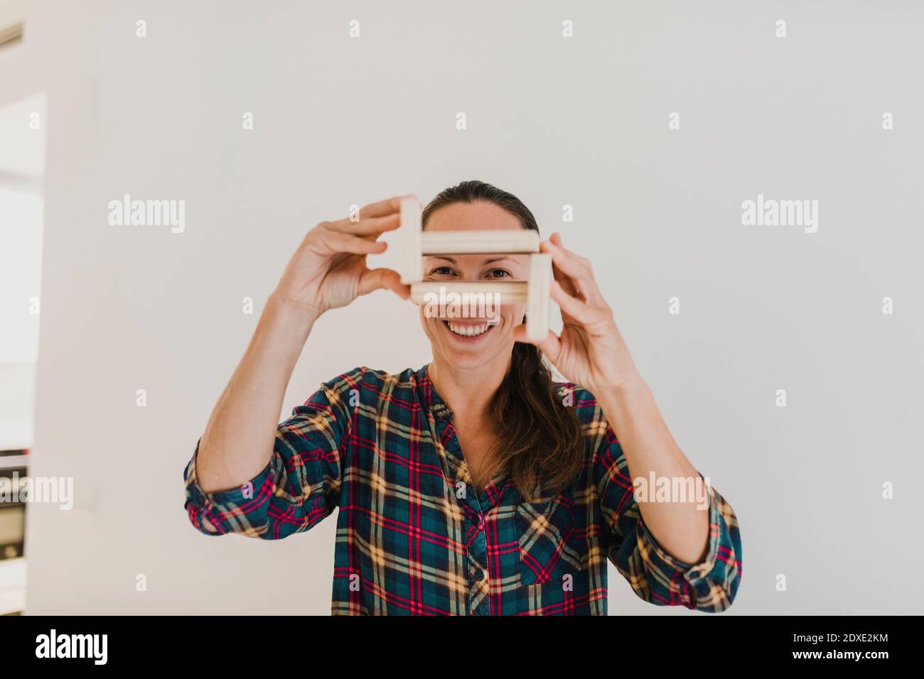 Lächelnde Frau, die durch Holzobjekt schaut, während sie zu Hause steht Stockfoto