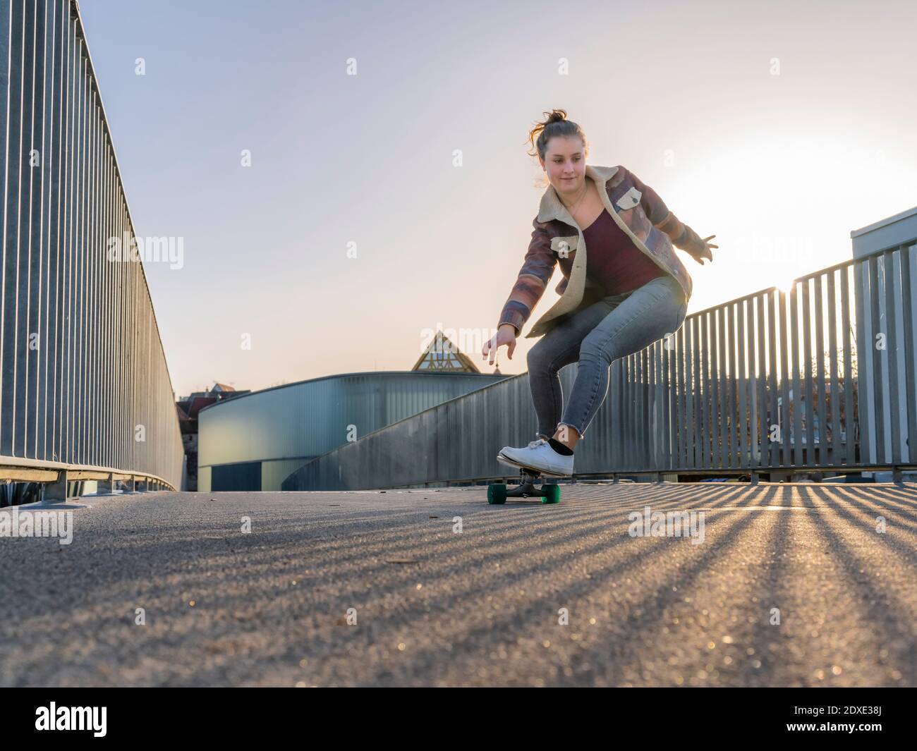 Junge Frau Skateboarding auf Fußgängerbrücke in der Stadt gegen klaren Himmel Stockfoto