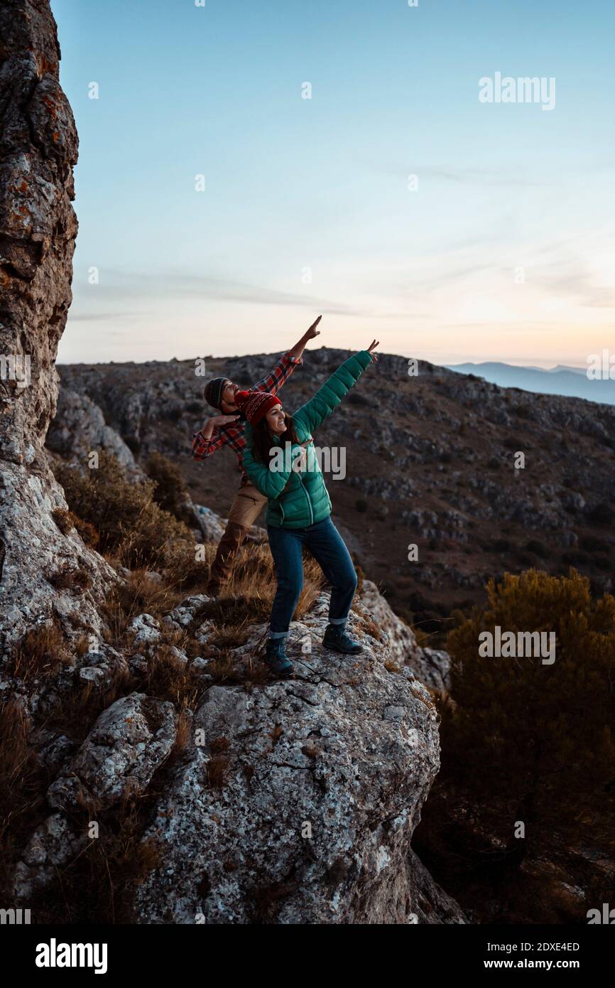 Glückliches Paar tanzt auf felsigen Berg beim Wandern gegen den Himmel Stockfoto