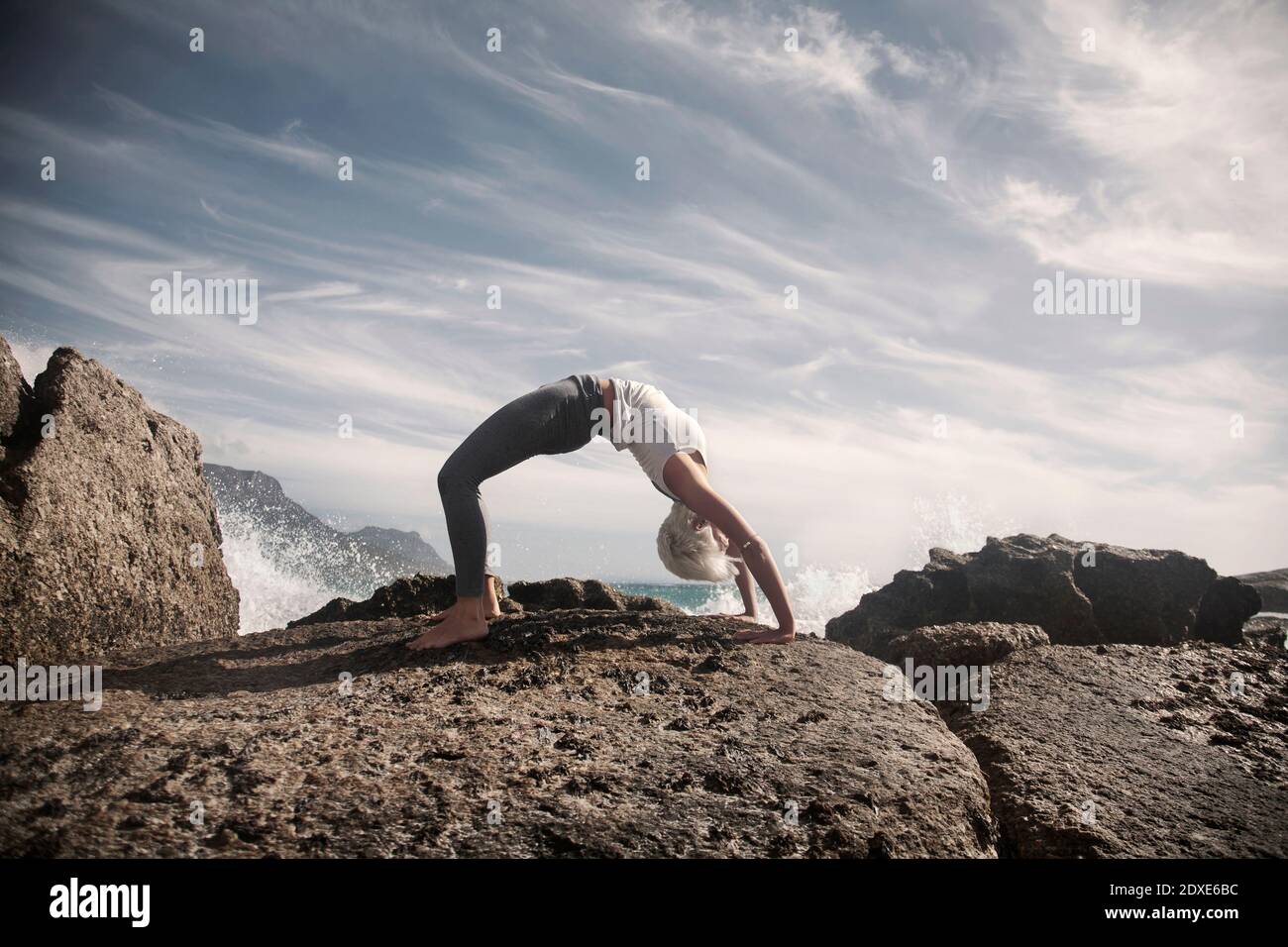 Flexible Frau üben Brücke Pose auf Felsformation am Strand Stockfoto