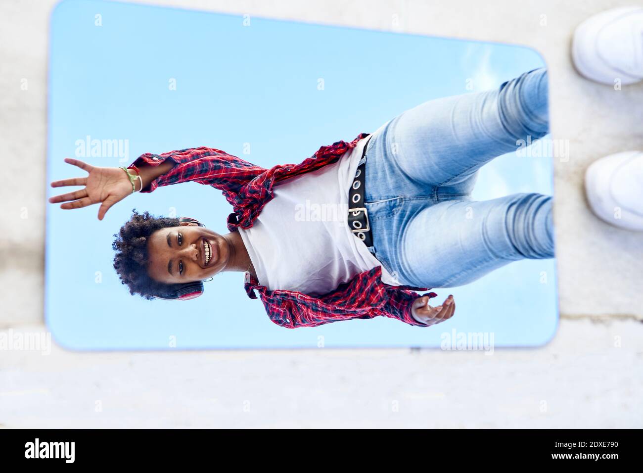 Verspielte junge Afro-Frau winkt vor Spiegelreflexion Stockfoto
