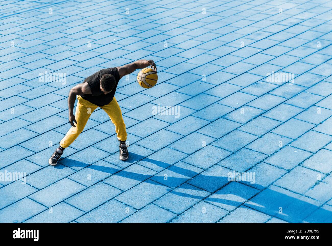 Junger Mann spielt Basketball auf blauem Bürgersteig Stockfoto