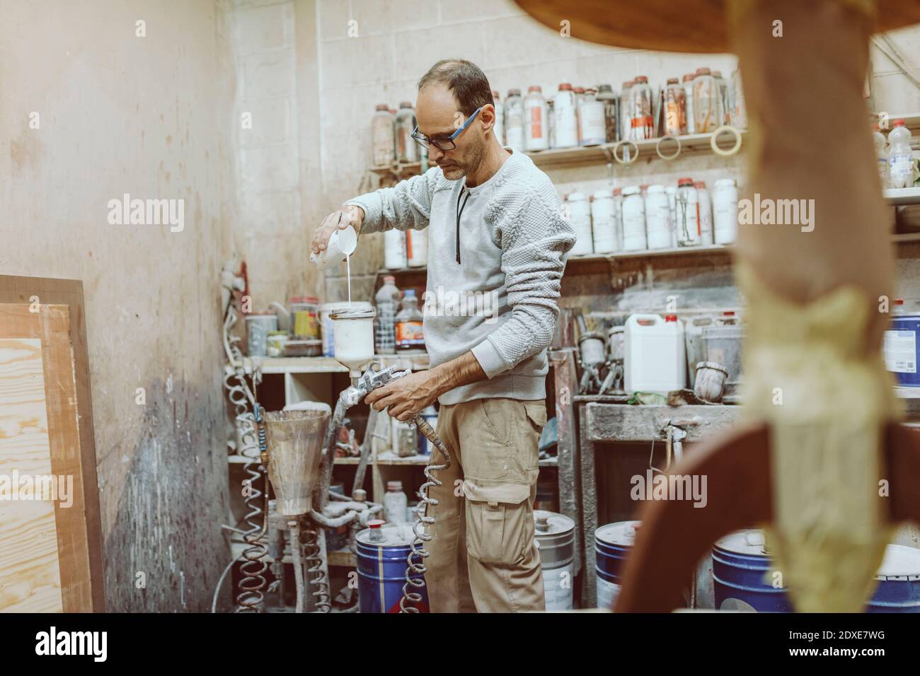 Manueller Arbeiter, der im Stehen weiße Farbe in die Spritzpistole setzt In der Werkstatt Stockfoto