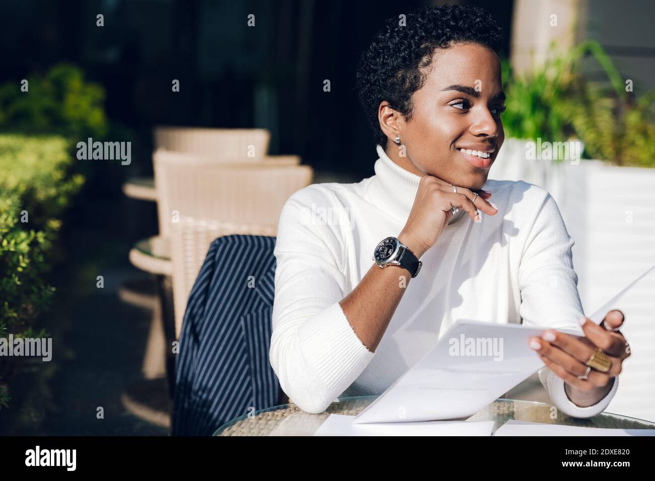 Lächelnde Geschäftsfrau, die wegschaut, während sie die Speisekarte im Restaurant hält Sonniger Tag Stockfoto