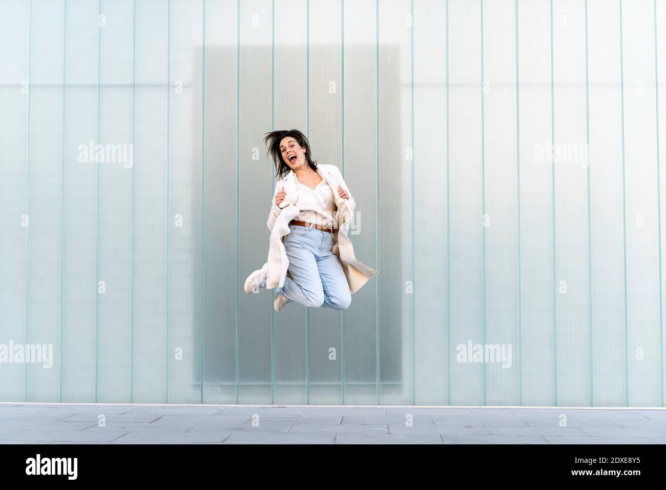 Fröhliche Unternehmerin springt mitten in der Luft gegen die Glaswand Stockfoto