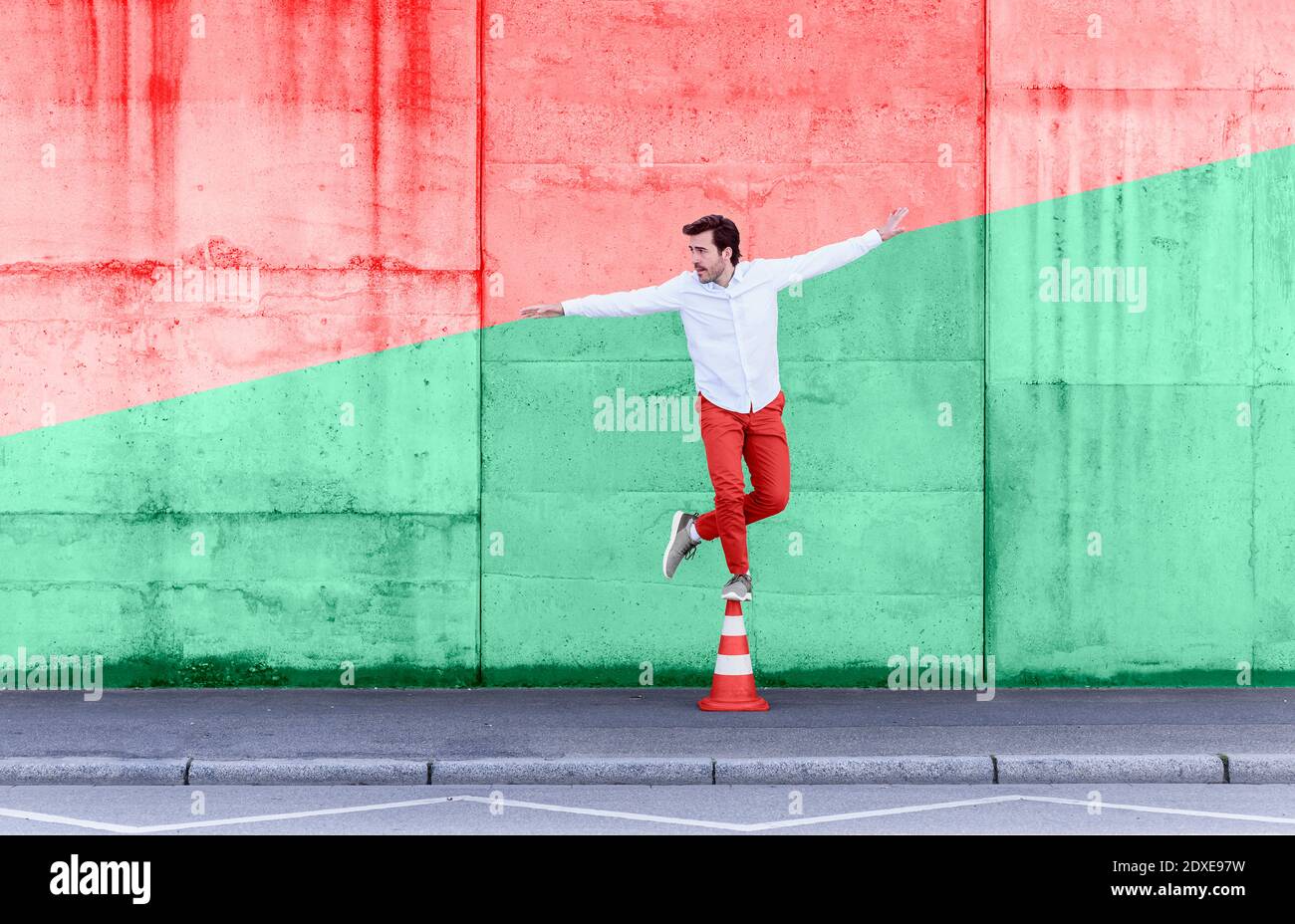 Sorgloser Mann, der auf dem Verkehrskegel gegen die vielfarbige Wand steht Stockfoto