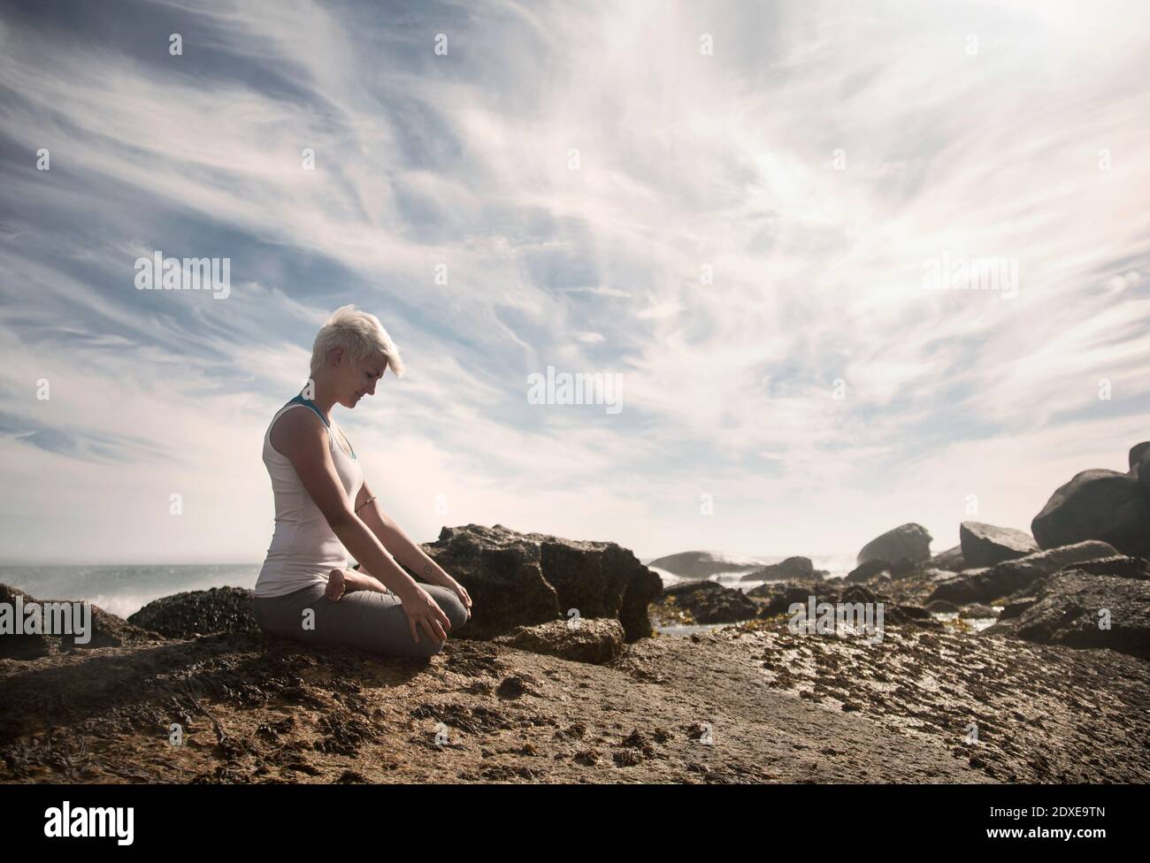 Frau meditiert während sie Lotusposition Yoga auf Felsformation praktiziert Am Strand Stockfoto