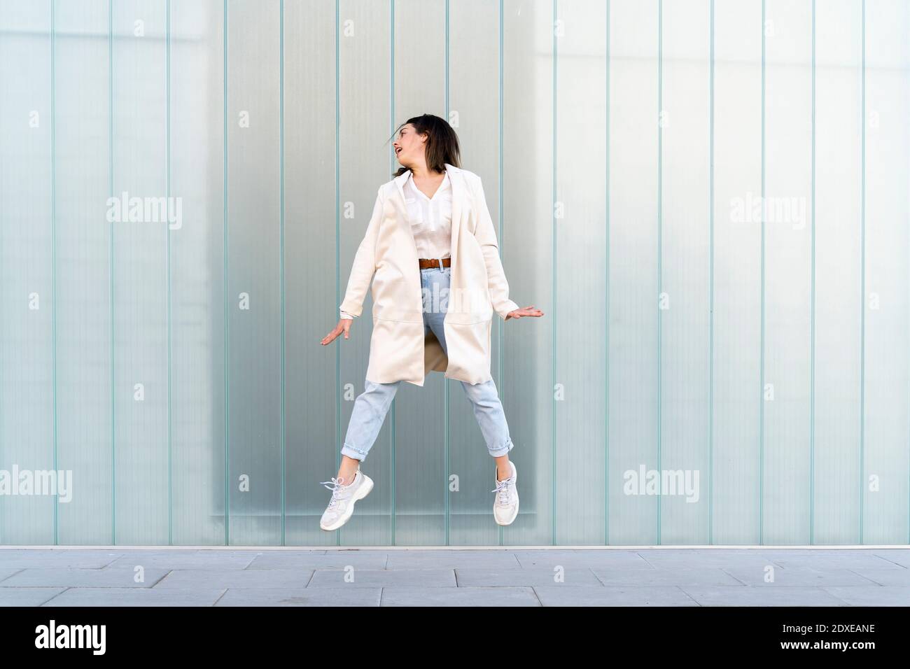 Unternehmerin springt mitten in der Luft gegen die Glaswand Stockfoto