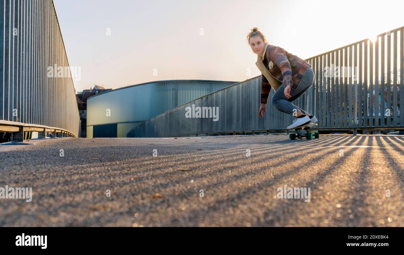 Sorglose junge Frau Skateboarding auf Fußgängerbrücke gegen klaren Himmel an Sonnenuntergang Stockfoto