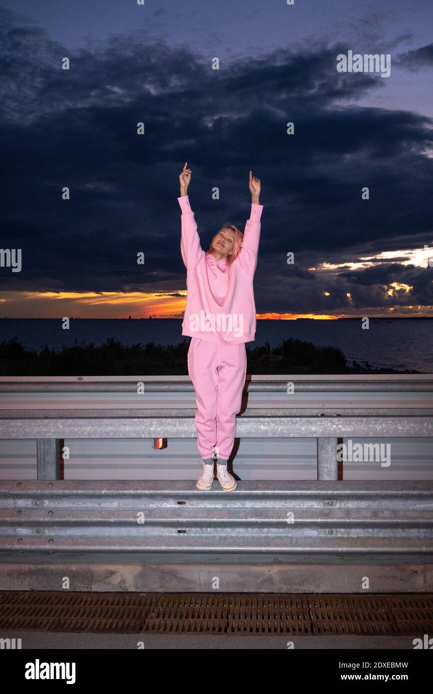 Junge Frau mit rosa Haaren trägt rosa Track Suit Shirt In der Dämmerung auf der Straßensperre stehen Stockfoto