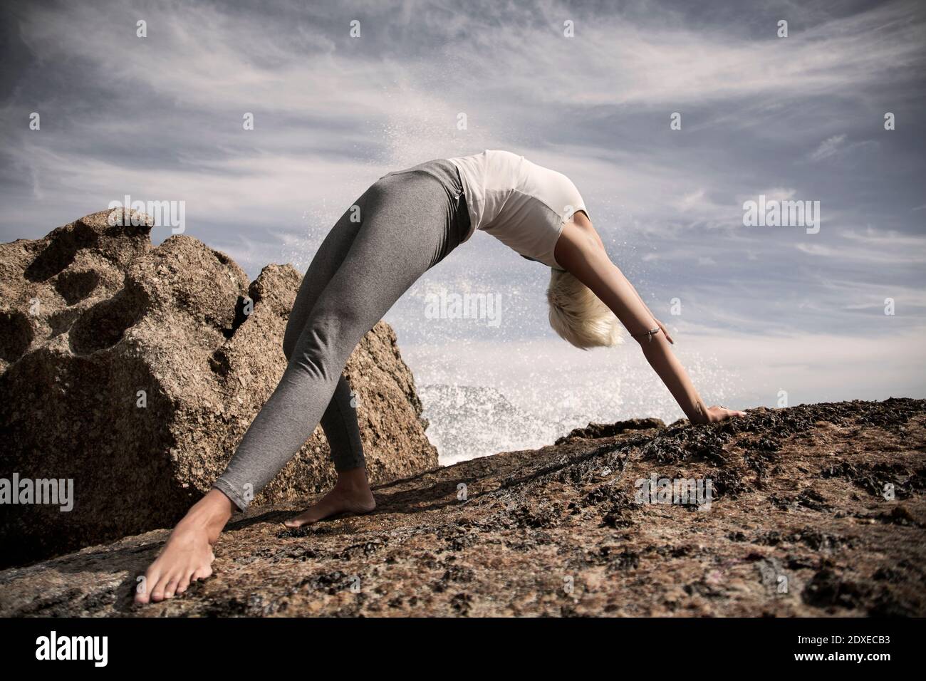 Flexible Frau praktiziert Yoga auf Felsformation am Strand Stockfoto