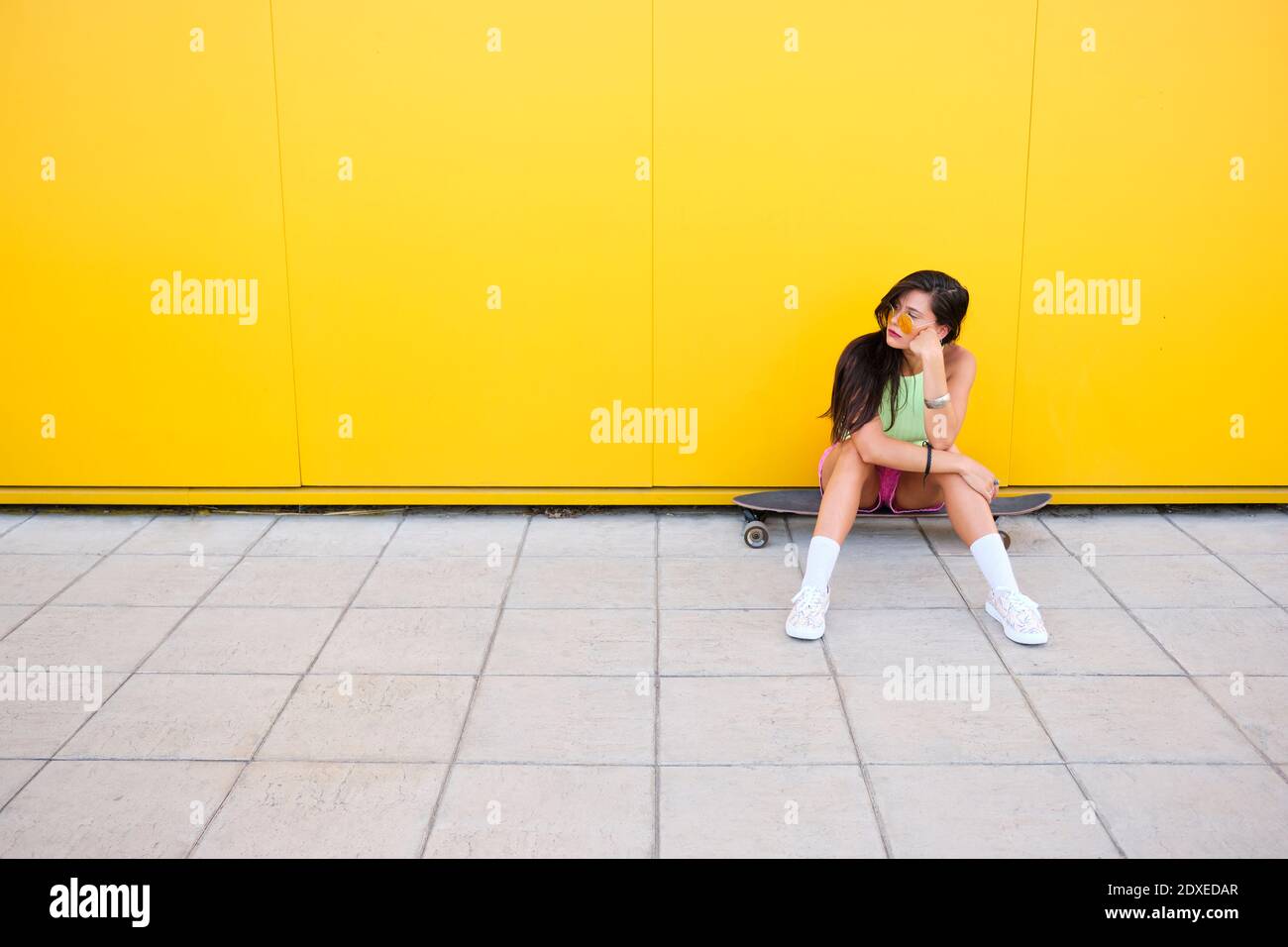 Portrait von schönen Mädchen allein auf Longboard vor gelb sitzen Wand Stockfoto