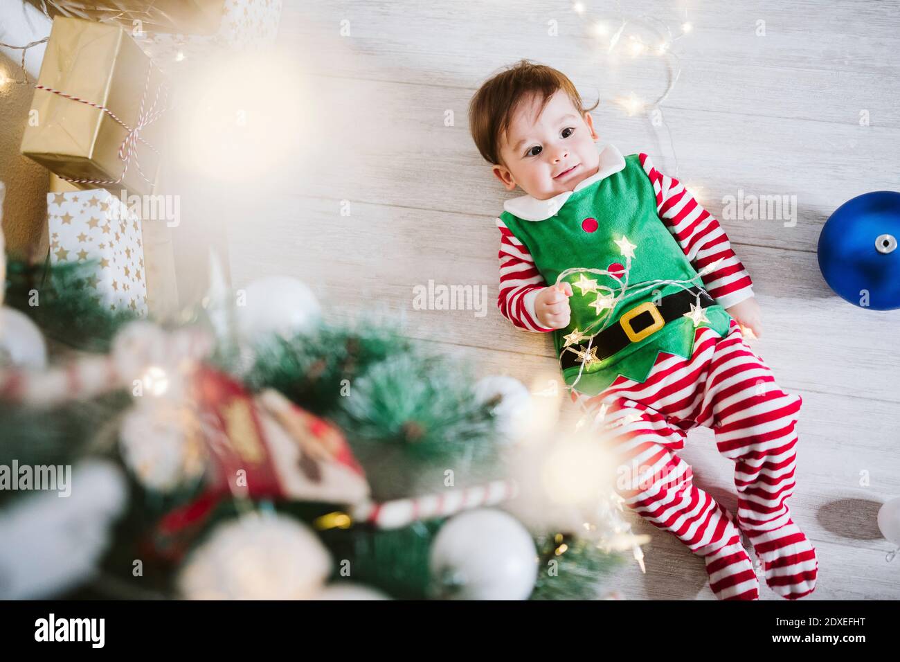Baby Junge in Elf Kostüm spielt mit String Licht während Zu Hause zu Weihnachten auf dem Boden liegen Stockfoto