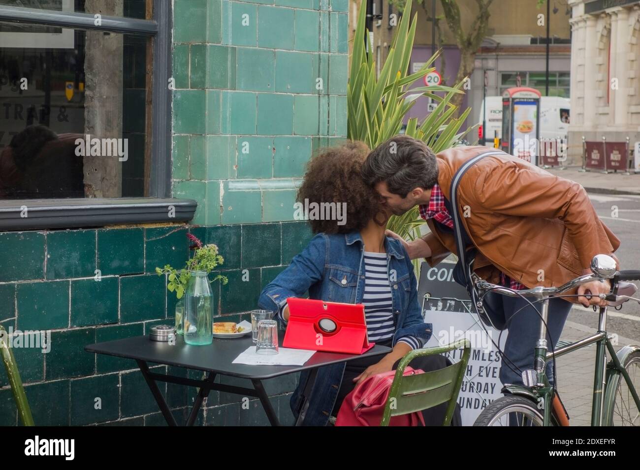 Mann auf dem Fahrrad Gruß junge Frau außerhalb eines Cafe Diner, London, UK sitzen Stockfoto