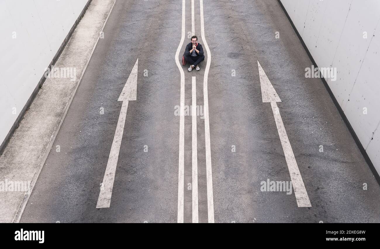 Junger Mann sitzt auf der Straßenmarkierung Stockfoto