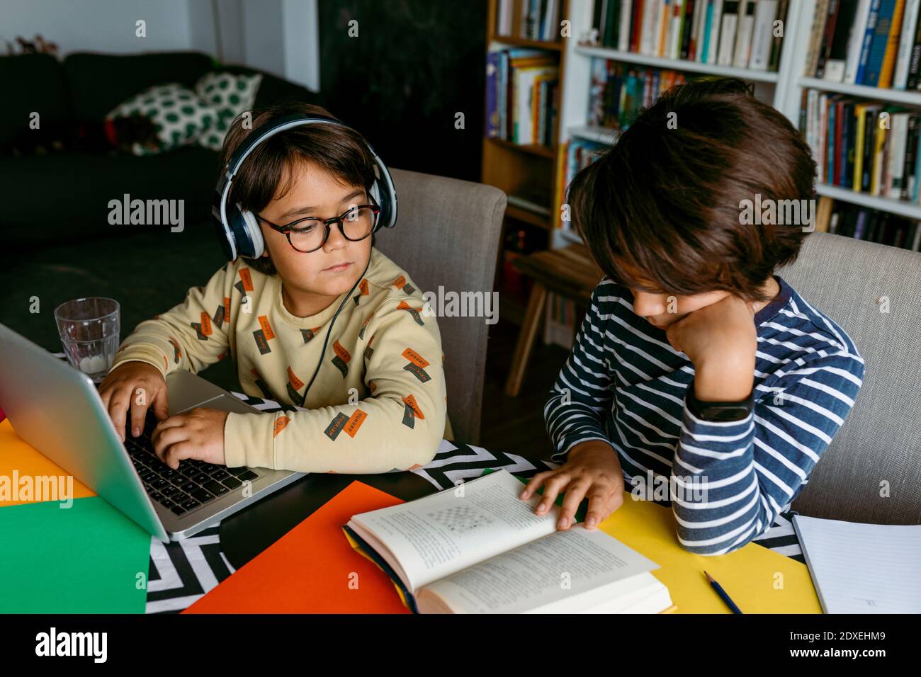 Junge guckt, während männliche Freund Lehrbuch am Tisch liest Stockfoto