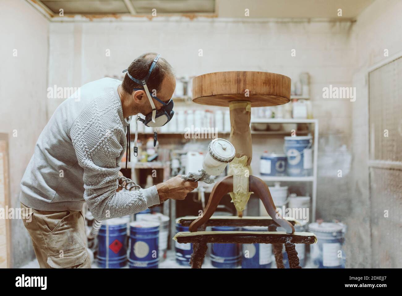 Männlicher Zimmermann mit Farbspritzpistole auf dem Tisch während der Arbeit In der Werkstatt Stockfoto