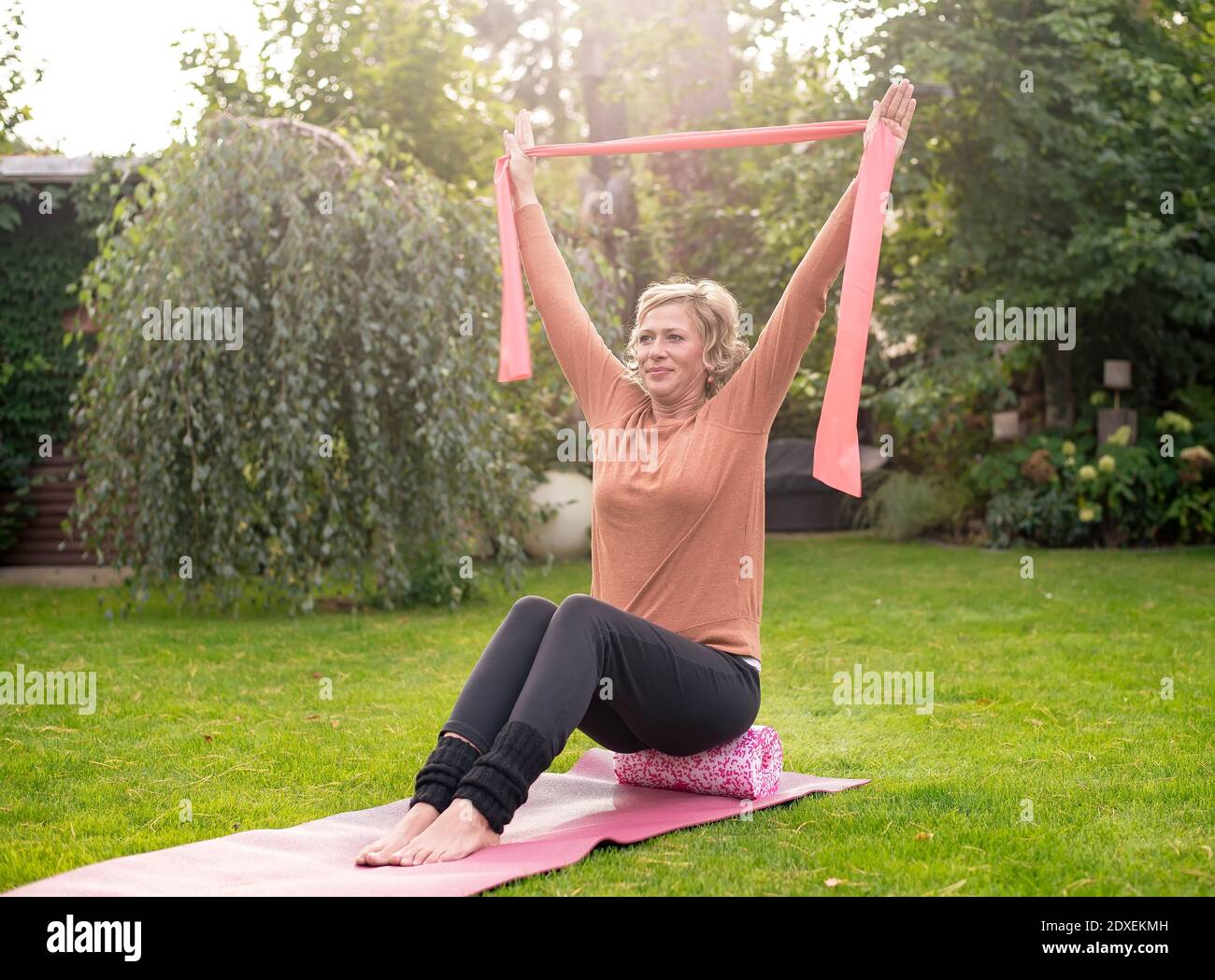 Frau, die mit Widerstandsband beim Rollen auf Schaumstoffrolle trainiert Im Hinterhof Stockfoto