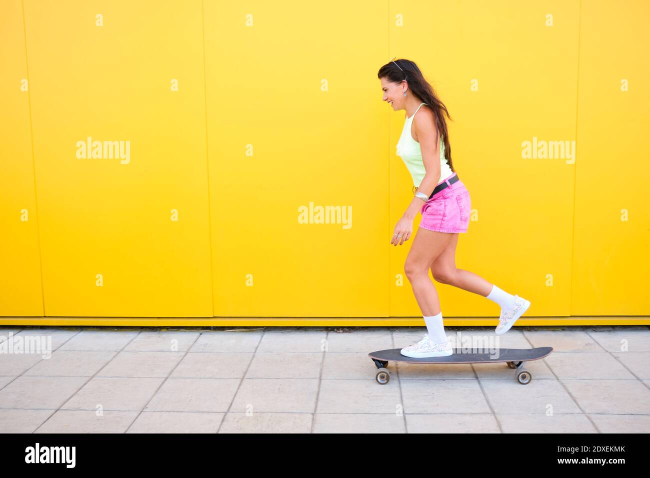Schöne Mädchen Skateboarding entlang gelbe Wand im Sommer Stockfoto