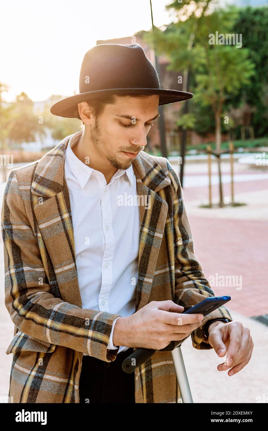 Geschäftsmann in Hut und karierte Jacke Blick auf Smartphone In der Stadt Stockfoto