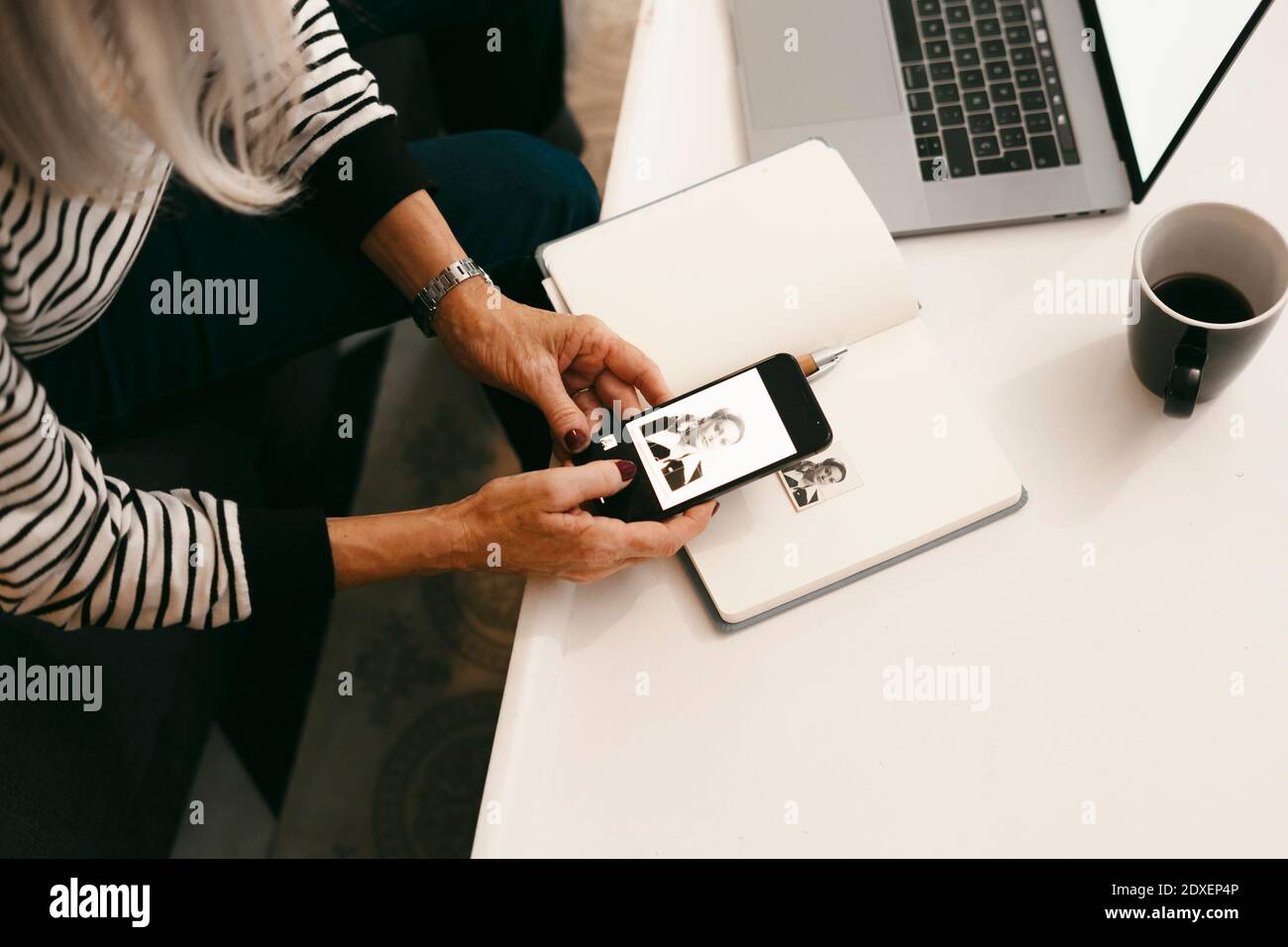 Ältere Frau, die ein Foto von Schwarz-Weiß-Foto auf Buchen Sie über das Mobiltelefon zu Hause Stockfoto