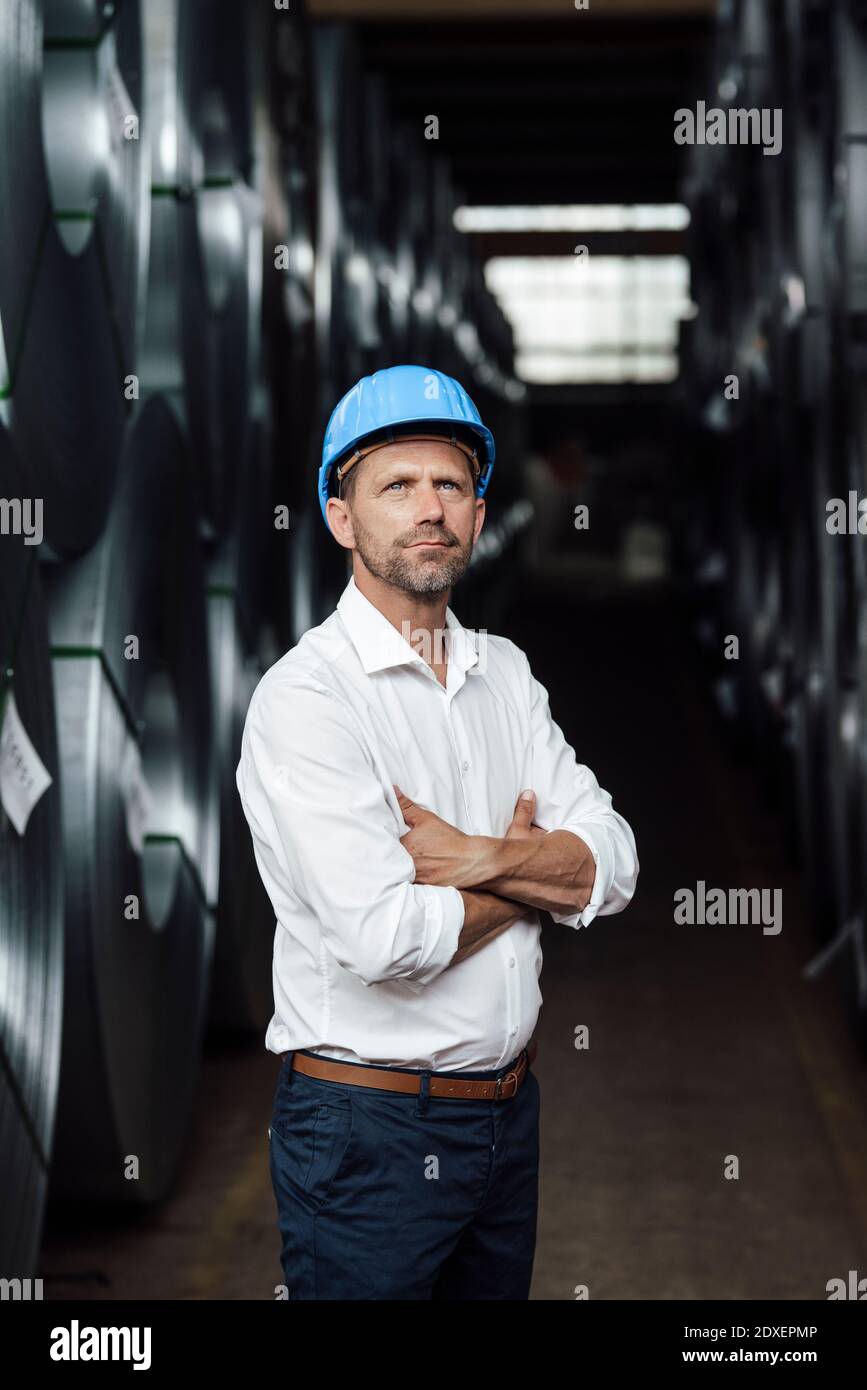 Geschäftsmann, der mit gekreuzten Armen, die von Stahlrollen durchzogen sind, nachdenkt Werk Stockfoto