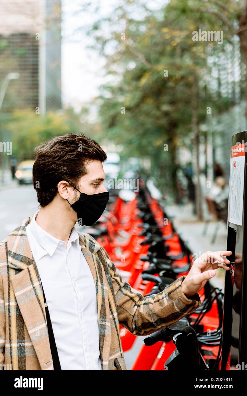 Junger Mann in Gesichtsmaske Fahrrad mieten in der Stadt Stockfoto