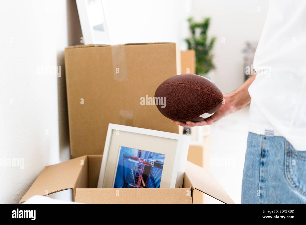 Mann hält Rugby Ball in der Hand beim Auspacken in neue Wohnung Stockfoto