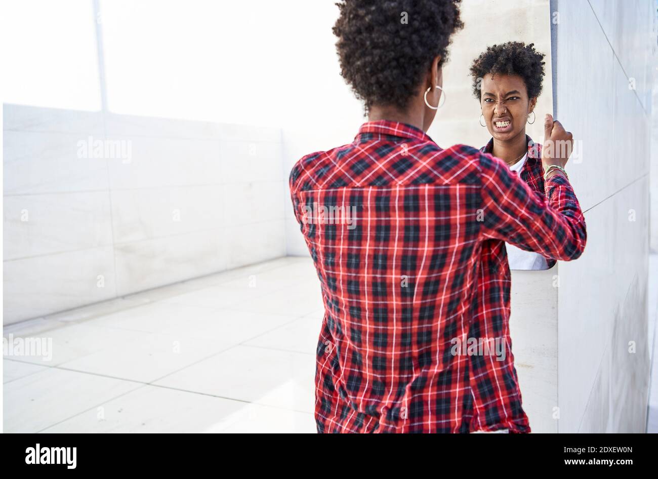 Junge weibliche Hipster macht ein Gesicht, während Blick auf Spiegel Spiegelung an der Wand Stockfoto