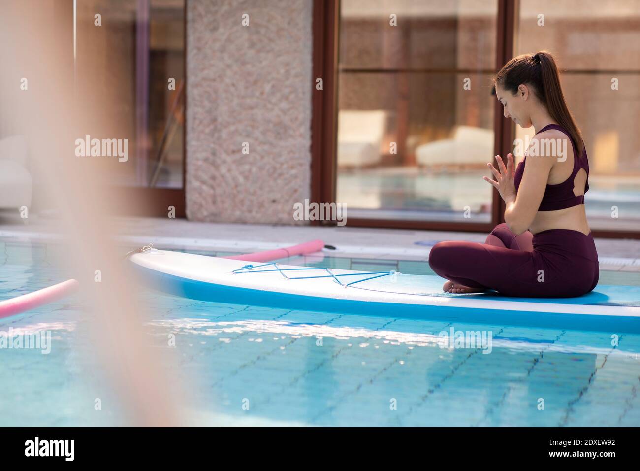 Weibliche Ausbilderin, die Yoga auf dem Paddleboard über dem Swimmingpool praktiziert Stockfoto