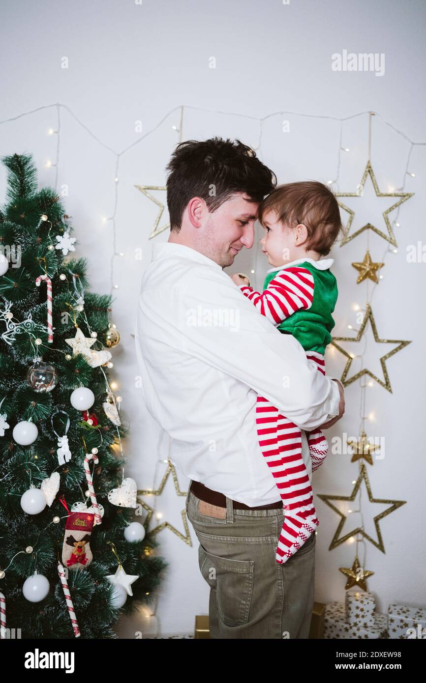 Vater umarmt Sohn trägt Elf Kostüm, während zu Hause stehen Zu Weihnachten Stockfoto